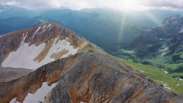 Tiro aéreo da montanha marrom-cinza cobriu a neve no belo vale de montanhas, coberto de florestas selvagens densas abaixo de nuvens e raios solares do sol de manhã. Vista superior da paisagem das montanhas — Vídeo de Stock