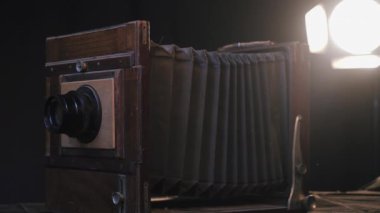 İzole edilmiş karanlık stüdyo odasındaki masanın üzerindeki klasik ahşap retro kameranın yakın çekim görüntüsü, ışık saçan lambanın arka planı. Yenileme, antika onarımları, eski moda fotoğraf ekipmanları..
