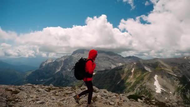 Vista lateral de mujer caminando turista conquistado y escalado pico en chaqueta naranja y mochila, deteniéndose y mirando con placer en el hermoso paisaje de montaña de las montañas del Cáucaso bajo las nubes . — Vídeo de stock