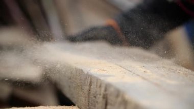 Elektrikli dairesel bir makineyle testereyle talaşın uçurulduğu kalın tahtanın yakın görüntüsü. Eldivenli bir adam öğütücü tarafından kesildikten sonra odun parçasından talaş topluyor..