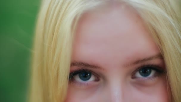 Nahaufnahme von attraktiven Gesicht und atemberaubenden blauen Augen von charmanten jungen kaukasischen blonde Frau mit anmutigen und verführerischen Blick auf dem Hintergrund des Grases. Schöne grüne Augen eines hübschen jungen Mädchens. — Stockvideo