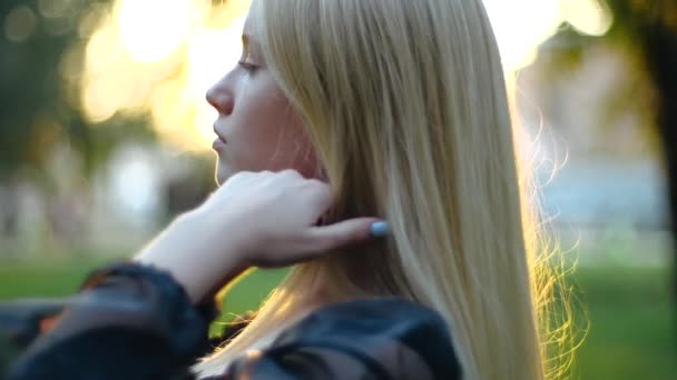 Крупный план съемки потрясающей молодой блондинки в легком платье пушистые длинные волосы против весеннего парка в солнечную погоду. Красивая девушка с ярким маникюром наслаждается теплой весной в уютном городском парке . — стоковое видео