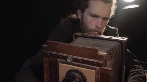 L'uomo barbuto accuratamente restaura attrezzature di fotografia retrò vecchie, aggiusta l'obiettivo, guarda la macchina fotografica di legno con sorriso gode la riparazione che sparge mani in piacere. Riparazione antica fotocamera obsoleta in camera isolata. — Video Stock