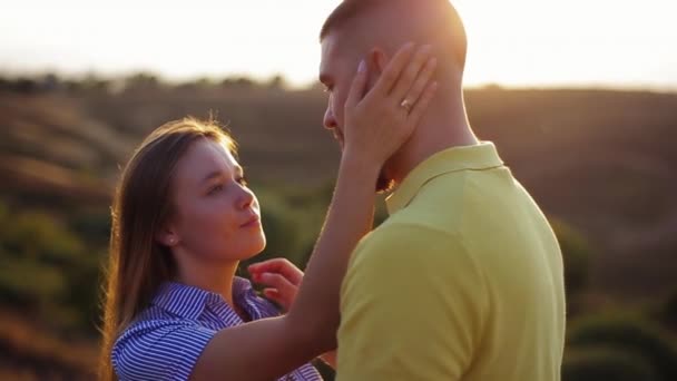 Vista da vicino della bella ragazza europea con lo sguardo amorevole accarezzando il viso del ragazzo barbuto, abbracciandosi appoggiato a lui sullo sfondo del tramonto sfocato al rallentatore. Data romantica della giovane coppia all'alba — Video Stock