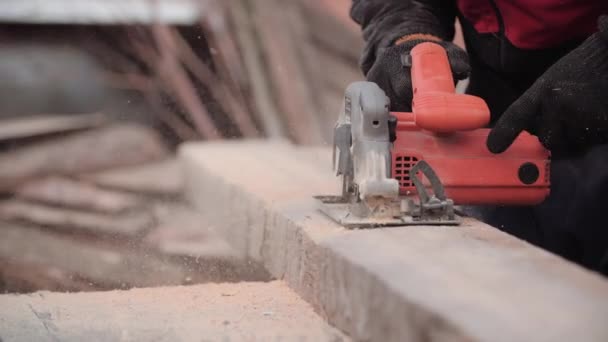 El proceso de trabajo del automóvil moderno circular de madera del trabajador no identificado en los guantes sobre el fondo borroso de las tablas en la calle, la vista de cerca en cámara lenta. Hombre corta pieza de madera usando amoladora eléctrica . — Vídeo de stock