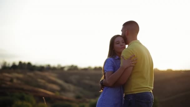 Happy menina atraente abraços barbudo menino amigo, beija-o, desfocado pôr do sol fundo. Prazer de férias romântico de par jovem no amor em conjunto na natureza. Reunião após a separação, menina obrigado cara — Vídeo de Stock