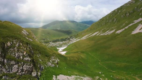 Lembah udara ditembak dan lereng pegunungan Kaukasus yang indah, ditutupi dengan rumput hijau padat, batu salju di bawah sinar matahari dan awan langit. Terbang di atas gunung yang menakjubkan Oshten Lago-Naki Plateau — Stok Video