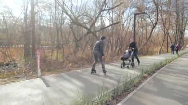 Jovem pai e mãe alegre em patins e seu bebê em um carrinho de criança no outono. Papai anda para trás e executa truques de salto. Educação desportiva e paixão saudável. Vida activa. Bom tempo. . — Vídeo de Stock