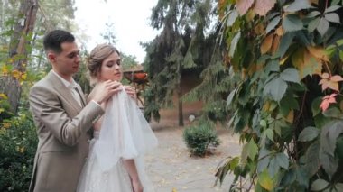 Doğada mutlu bir Avrupalı düğün çifti var. Damat geline sarılıyor ve gelinliğini omzuna dayayıp köknar ağaçlarının ve ormandaki bir evin arka planına dayanıyor..