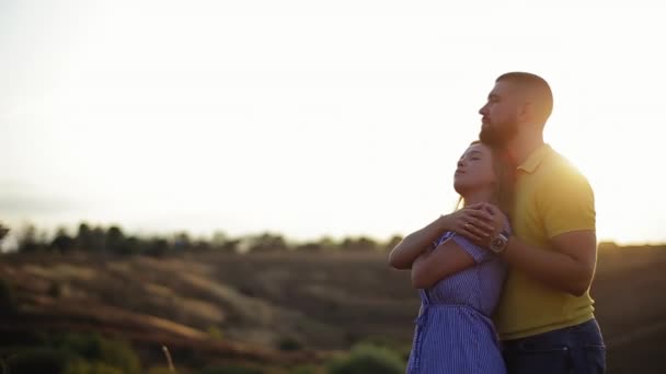 Romantique jeune couple dans l'histoire d'amour. Un barbu embrassant sa copine au coucher du soleil dans un champ désert. Concept de date avec un être cher ensemble dans la nature. Garçon fort étreint sa fille heureuse par derrière — Video