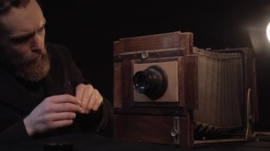 Aktif sakallı bir adam gülümseme ve şevkle eski antika retro kamerayı, fırçayla temiz lensi onarır ve lambanın ışığı altında karanlık odada işlemden zevk alır. Antika teçhizat onarımı