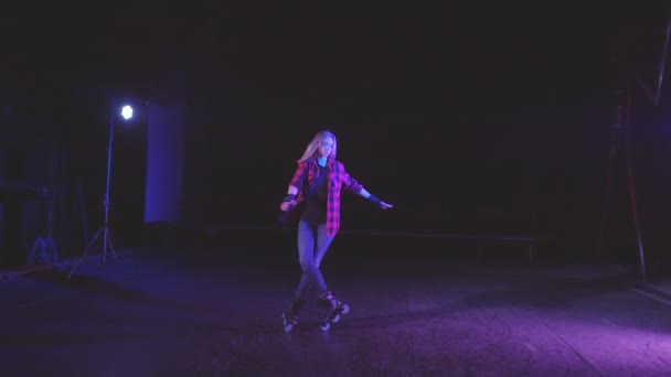 Nice young blonde girl spinning and making U-turns on rollers in place on front wheels against bright blue pink spotlight on scene of abandoned building in panoramic shot. Active lifestyle and sport. — Stock Video