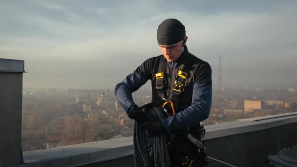 Berufskletterer steht in Uniform auf dem Dach und entwirrt ein Sicherungsseil, um draußen die Hauswand herunterzulassen. Riskante und gefährliche Arbeit für das Leben. Extremsport für Männer. — Stockvideo