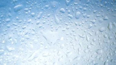 Güneş ışınlarındaki su saflığı sıvısı mavi gökyüzünden düşer. Güzel lekeler, şeffaf cam arka planda su damlaları. Kozmetik prosedürler ve ürünler, tazelik, nem, koruma ve bakım konsepti