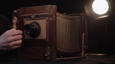 Bir el sakallı adam, izole edilmiş stüdyoda küçük bir fırçayla eski tip ahşap kameraların lenslerini masaların üzerine siliyor. Restorasyon, antika antika antika eski moda ekipmanlar karanlık odada.