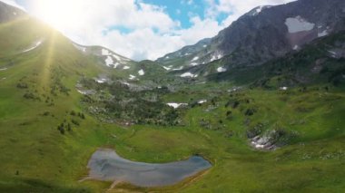 Yoğun çimenler, ağaçlar ve taşlarla kaplı, bulutların ve güneş ışınlarının buharı altında nefes kesen güzel dağların üzerinde uçuyor. Yaz mevsiminde sabah Alpler 'in hava manzarası. Dağ doğasının manzarası.