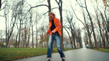 Orta yaşlı, formda, sakallı bir adamın Central City Park 'taki caddede kaykay yaparken, baharda ağaçların ve çimenlerin arasında, yağmurlu bir havada görüntüsü. Profesyonel scooter aldatmacaları ve dönüşleri gerçekleştirir