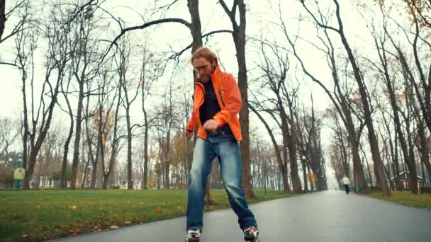 天気の良い春には木々や草に囲まれた都心の公園でローラースケートを楽しむ中年のひげそりの男のクローズアップビュー。プロのスクーターは、フェイントを実行し、ターン — ストック動画