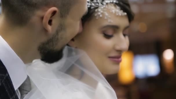 Vue rapprochée d'un beau couple de mariage embrassé à l'hôtel de luxe Kharkov Palace, Ukraine. Le marié barbu dit quelque chose à l'oreille de sa jolie mariée dans une robe blanche chic. Joyeuse lune de miel. — Video