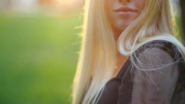 Vista de cerca de la cara linda y los labios encantadora chica rubia caucásica sonriente en vestido negro graciosamente corriendo dedo a través de su cabello, sonriendo a la cámara en el parque, se centran en la barbilla boca y hombro — Vídeos de Stock