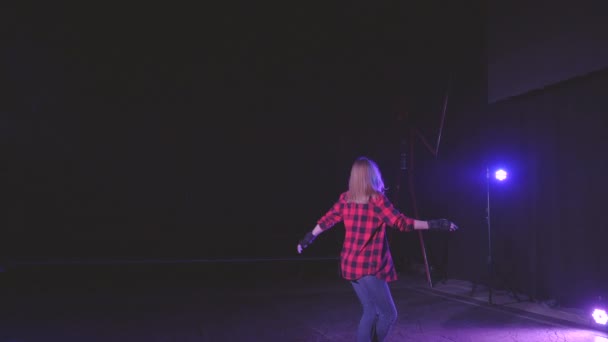 Blond rolmeisje met beschermende handschoenen, sierlijk wervelt op rolschaatsen op voorwielen in donkere studio onder neon roze blauw licht van schijnwerpers in slow motion. concept actieve sport levensstijl — Stockvideo