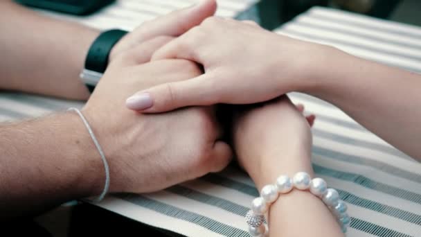 Vue rapprochée des mains lisses féminines avec manucure et bracelet en perles serrant et caressant les mains masculines avec montre sur la nappe rayée de la table de café. Rendez-vous romantique pour jeune petit ami et petite amie. — Video