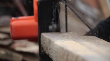 Bulanık arka planda, kalın tahta üzerinde çalışan dairesel makine, havada uçan talaş parçasına odaklanıyor, yavaş çekimde yakın çekim görüntüsü. Marangoz ahşap tahtada testere keser ve öğütücü keser..