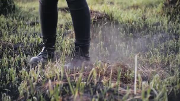 Menselijke benen in stijlvolle leren schoenen draaien in een cirkel op ashen verbrand gras in slow motion bij zonnig weer. Persoon draait op de verbrande aarde in een veld overdag, rook waait na een brand. — Stockvideo