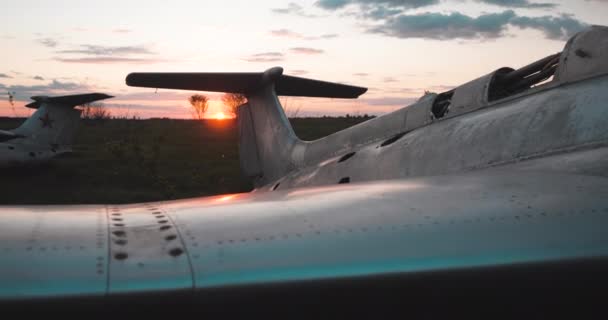 Detaljerad bild av vinge, flygkropp och svans sovjetiska militära stridsplan i fält mot solnedgången. Gammal flygfält med flygplan bombplan av Sovjetunionen. Flygplats kyrkogård i öde fält på kvällen. — Stockvideo