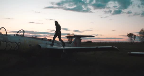Actieve energieke man rent rond de oude Sovjet militaire strijders van de USSR en bespringt ze een voor een op de luchthaven in de avond, zijaanzicht in slow motion. Toerist bezig met parkour op het vliegtuig. — Stockvideo
