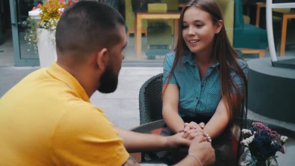 Close-up view of romantic date of young smiling cute couple in love sit in modern cafe at table outside, holding hands enjoying conversation. Beautiful girl spends leisure with beloved in restaurant. — Stock Video