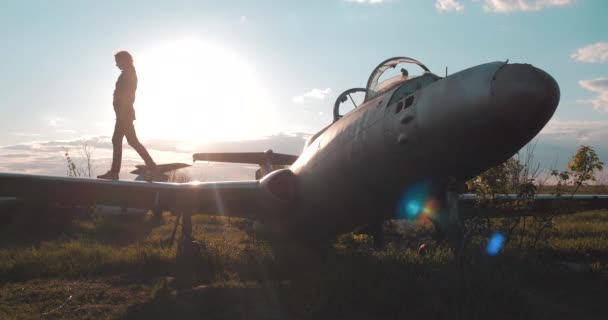 Vista média da menina turista andando ao longo da asa do avião de combate soviético quebrado, em seguida, virar e jogar a cabeça para trás de desfrutar no aeródromo perto do transporte histórico, fundo do sol . — Vídeo de Stock