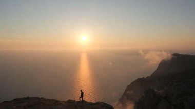 Karadeniz 'in yukarısındaki yüksek bir dağın kenarında duran aktif bir turistin siluetinin hava görüntüsü. Bir dağdaki uçurumun kenarındaki bir turist sonbaharda günbatımında büyüleyici bir manzaranın tadını çıkarır..