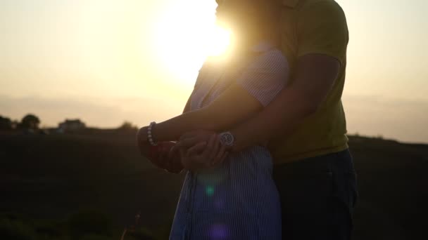 Close-up uitzicht op twee liefhebbers genieten van romantische avond buiten in de open lucht. Guy knuffelt meisje van achteren op de achtergrond van zonsondergang in het veld in slow motion. Begrip actief vrijetijdsbesteding en samen uitgaan. — Stockvideo