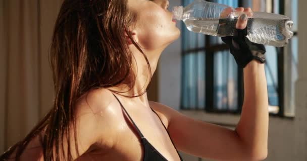 Nahaufnahme von Gesicht und Brust schöne hübsche kaukasische Frau mit Make-up löschen Durst mit Vergnügen trinken Wasser in Flasche in Hitze nach dem Training in isolierten weißen Turnhalle gegenüber Sonne vor dem Fenster.