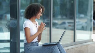 Heyecanlı genç Afrikalı kadın başarıyı kutluyor iyi haberler alıyor, laptopta mesaj yazıyor, el sallıyor. Beklenmedik bir sevinçten şaşkın kız içgörüden, mutlu yüz ifadesinden hoşlanıyor.
