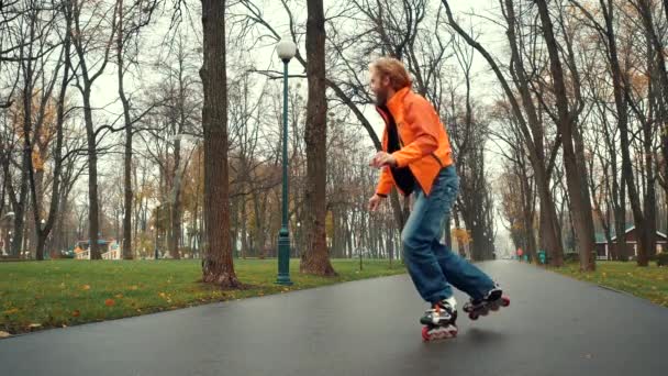 Sonriente y feliz hombre barbudo disfruta del patinaje sobre ruedas, hace varios giros técnicos y fintas en el callejón de Gorky Park, Kharkov, Ucrania. Patinador experimentado pasa deportes y ocio activo al aire libre . — Vídeos de Stock
