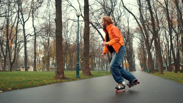 Usmívající se a šťastný vousatý muž má rád bruslení na kolečkových bruslích, dělá různé technické zatáčky a finty v uličce Gorky Park, Charkov, Ukrajina. Zkušený bruslař tráví sportovní a aktivní volný čas venku. — Stock video