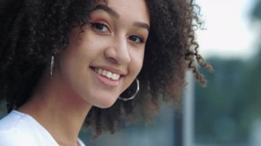 Güzel Afro-Amerikan milenyum kadınlarının yakın plan fotoğrafları. Mutlulukla gülümsüyorlar. Kameraya neşeyle göz kırparcasına göz kırpıyorlar. Güzel, kıvırcık saçlı, pozitif bir kız..