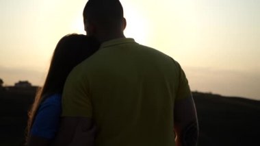 Birbirlerine aşık genç çiftlerin arka planda el ele tutuşup gün batımının arka planında el ele tutuşmaları. Romantik randevu kavramı. Temiz havada aşk. Güçlü erkek ve kız doğada güzel bir akşamın tadını çıkarıyorlar.