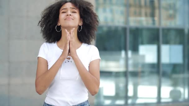 Jonge Afro-Amerikaanse vrouw maakt wens, kruist middelste en wijsvingers op handen, bidt gebalde handen in smekend gebaar. Droom is uitgekomen, meisje stuitert in extase, lacht vrolijk springend. — Stockvideo