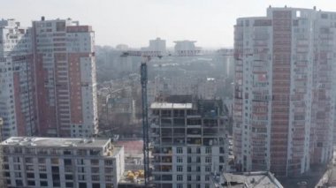 Şantiyedeki modern uzun evlerin arka planına karşı çeşitli ofis ve konut binalarıyla aktif bir şehir inşaatının havadan çekimleri. Crane ve işçiler çatıda..