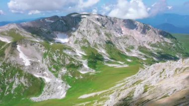 Beyaz bulutların altında kar taşları ve çimlerle kaplı Kafkasya 'nın görkemli doğasının Oshten tepesinden Mountain Fisht' e kadar uzanan hava manzarası. Güneş yazın ışıldıyor, Adygea, Rusya
