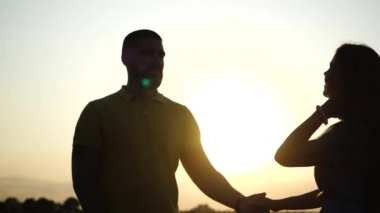 Mutlu genç adam ve kız, doğada romantik bir akşamın tadını çıkarıyorlar. El ele tutuşuyorlar ve yaz günbatımının arka planında yavaş çekimde dans ediyorlar. Açık havada aşık çiftlerin randevusu..