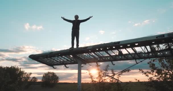 Feliz homem sorridente com uma barba está de pé na asa de um pequeno avião abandonado com os braços estendidos e levantados contra o pano de fundo do pôr do sol de verão. Inspirado turista sobe veículo voador . — Vídeo de Stock