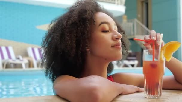 Afroamerikanerin auf Reise Sommerurlaub Baden in Malediven Hotelpool trinken Luxus-Saft-Cocktail kokettiert fröhlich lächelnd. Tropisches Wochenende entspannen erfrischendes Wasser mit gesundem Getränk, Porträt — Stockvideo