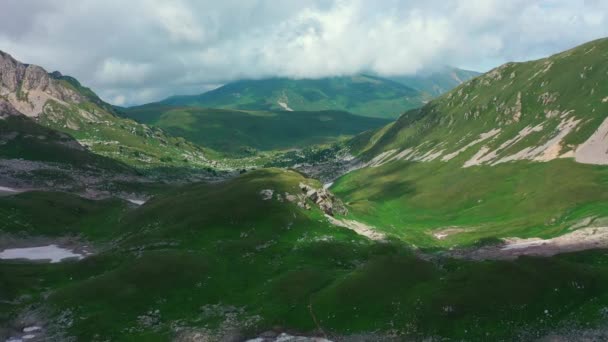 Повітряний вид на долину серед прекрасних гір Кавказу, приголомшлива ущелина, вкрита зеленою травою під плавучими тінями хмар. Переліт через епічні гори Риба Оштен Лаго-Накі плато, Росія — стокове відео