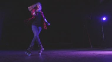 Yakın plan panoramik manzara, patenlerin üzerinde dönen güzel bir kız ön tekerlerin altında parlak spot ışıkları altında, terk edilmiş binanın peronunda, hızlandırılmış çekim alanında..