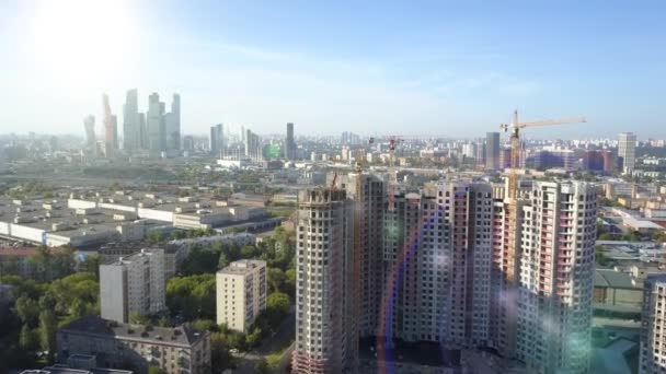 Aerial view of tall residential building under construction against the backdrop of the business business center of the city, a crane and skyscrapers under the bright sun in the spring season, Moscow. — Stock Video