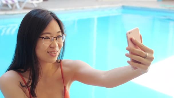 Primer plano feliz asiático etnia mujer en gafas haciendo foto retrato selfie en cámara teléfono gadget fuera de casa en la piscina o el uso de dispositivo de teléfono inteligente para la comunicación amigos en videoconferencia — Vídeo de stock